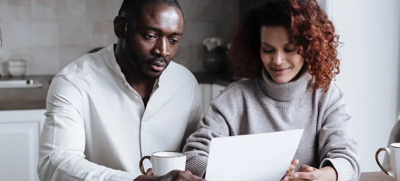 A couple at their kitchen table reading over mortgage paperwork together